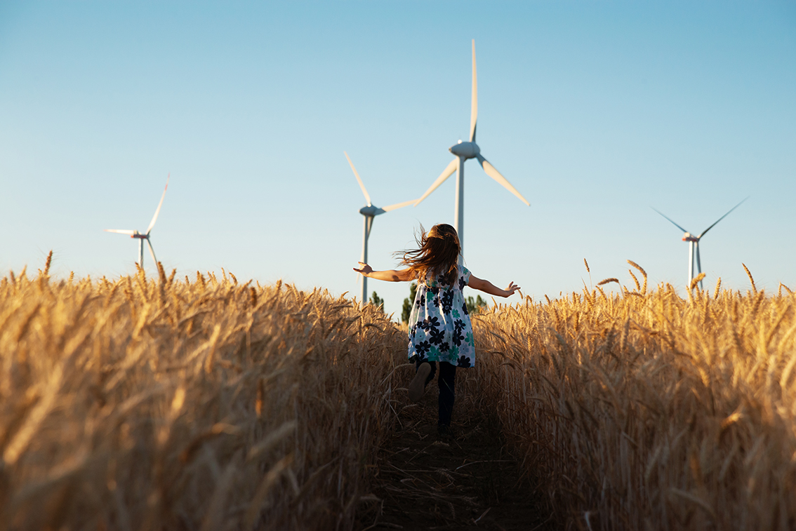 Mädchen läuft im Weizenfeld mit Windrädern im Hintergrund